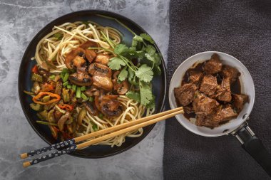 Çin Eriştesi mantar ile bir tavada, sebze ve otlar kızarmış et gri masada vardır. Üstten görünüm