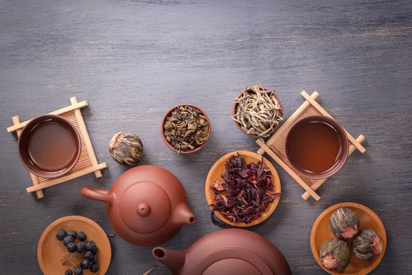 Several types of green tea, black tea, hibiscus tea and tea ceremony attributes - a ceramic teapot, cups, a strainer, chopsticks and tweezers are placed on an old wooden table. Top view Copy space