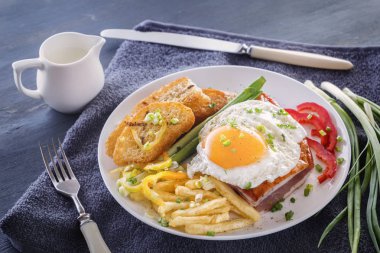 Sahanda yumurta pastırmalı kızarmış adet ekmek, yeşillik, domates ve patates kızartması gri bir ahşap masa üzerinde beyaz bir tabak içinde. Yakın çekim