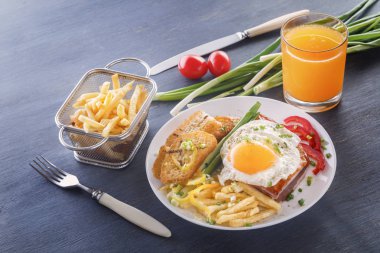 Sahanda yumurta beyaz bir tabak kızarmış adet ekmek, yeşillik, domates, patates kızartması ve bir bardak taze meyve suyu üzerinde gri bir ahşap masa ile pastırmalı. Yakın çekim