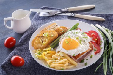 Sahanda yumurta pastırmalı kızarmış adet ekmek, yeşillik, domates ve patates kızartması gri bir ahşap masa üzerinde beyaz bir tabak içinde. Yakın çekim