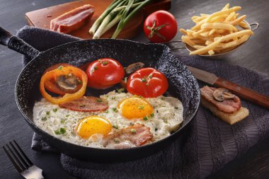 Patates kızartması gri bir tablo ile kızarmış yumurta pastırma ve dökme demir eski bir domates ile pan. Yakın çekim