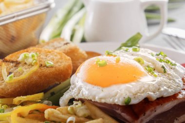 Bir tabak kızarmış adet ekmek, yeşil ve gri bir ahşap masa üzerinde Fransız kızartması ile pastırmalı kızarmış yumurta. Yakın çekim