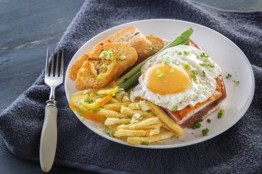 Bir tabak kızarmış adet ekmek, yeşil ve gri bir ahşap masa üzerinde Fransız kızartması ile pastırmalı kızarmış yumurta. Yakın çekim