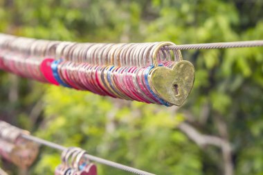 Bir yaya köprüsü çelik bir kablo üzerinde bir kalp şeklinde aşk kilitleri asmak