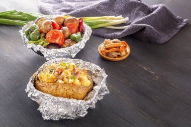 Fırında patates ile pastırma, soğan ve pişmiş sebze folyo - domates, patlıcan, biber üzerinde gri bir ahşap masa.