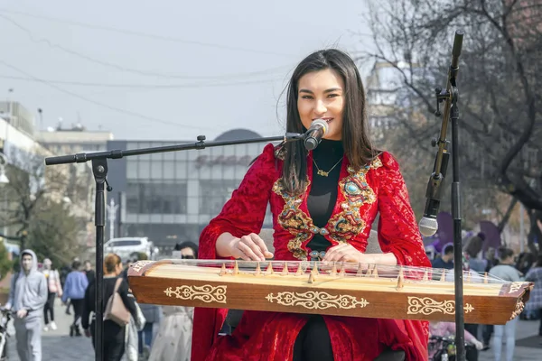 Vacker flicka i den nationella kazakiska kostymen spelar den folkliga musikinstrumentet Zhetygen på gatulivet firar Nauryz semester — Stockfoto