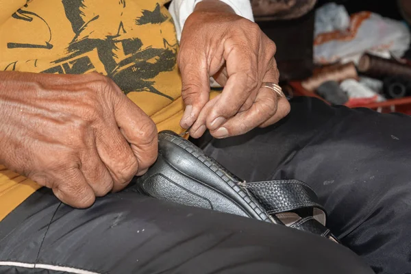 Bir ayakkabıcı ellerini sokak dükkanında eski sandalet sews. Close