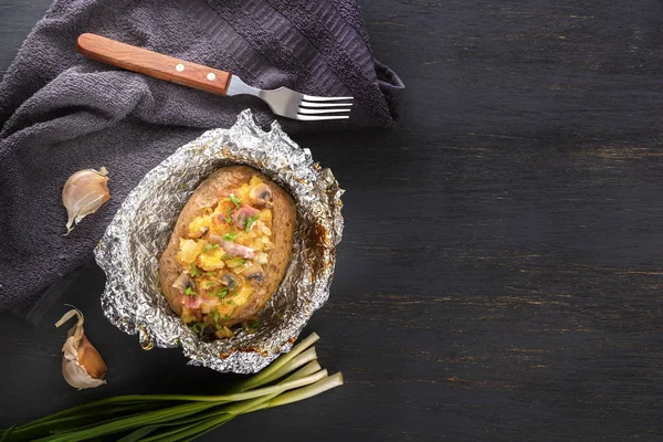 Domuz pastırması, soğan ve mantar ile folyo fırında patates gri ahşap masa üzerinde çatal ile. Boşluk Kopyala. Üst görünüm