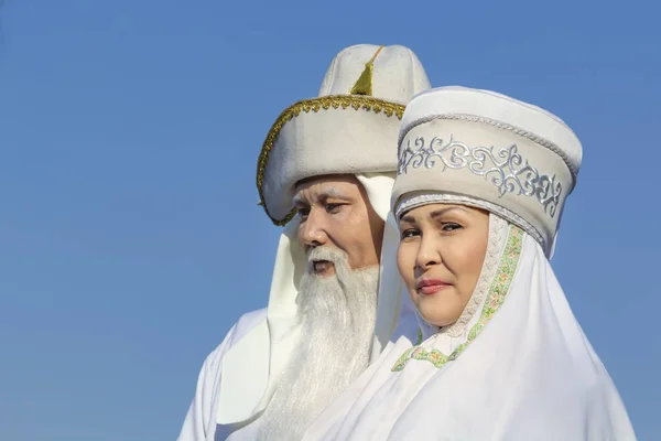 Almat, Kazakistan - 21 Mart 2019. Karnaval tatili sırasında gökyüzünün arka planına karşı beyaz ulusal Kazak giysileri yaşlı erkek ve kadın. Close. Portre