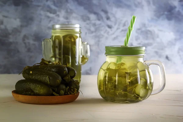 Pepino en vinagre en un frasco con tapa y tubo y pepinos en vinagre en un plato sobre una mesa de madera. Primer plano — Foto de Stock