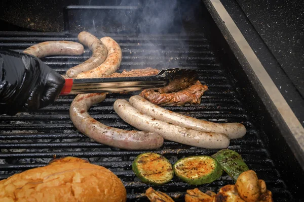 O cozinheiro coloca na grelha variada de carvão - salsichas, bife de carne, legumes e cogumelos. Comida de rua — Fotografia de Stock