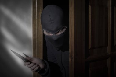 Elinde bıçak ve gözleri için bir yarık ile bir şapka ile Hırsız ay ışığında gece kapıdan eve gizlice