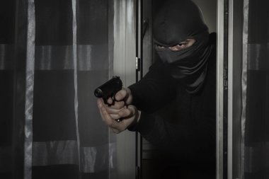 Elinde silah olan ve gözleri yarık bir şapka ile Hırsız ay ışığında gece kapıdan eve gizlice