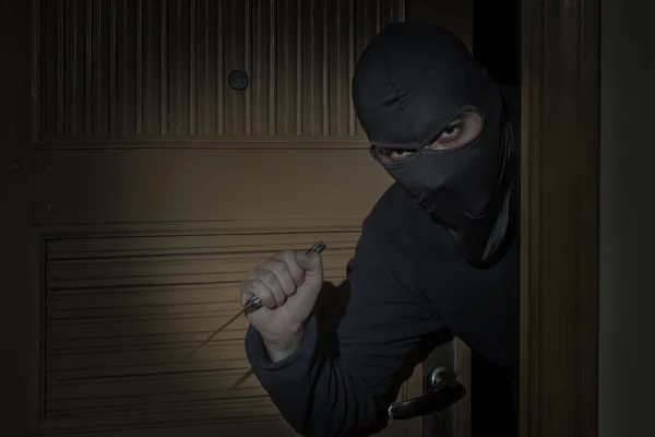 Ladro con un coltello in mano e un cappello con una fessura per gli occhi si intrufola in casa attraverso la porta di notte al chiaro di luna — Foto Stock