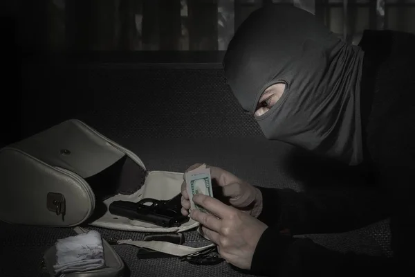 Robber in a mask and with a flashlight examines the contents of the women's bag in a dark room — Stock Photo, Image