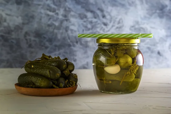 Cucumber pickle in a jar with a lid and tube and pickled cucumbers in a plate on a wooden table. Close-up