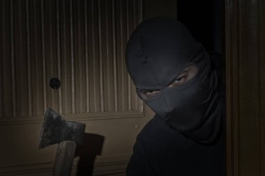 Elinde balta olan ve gözleri yarık bir şapkayla hırsız gece ay ışığında kapıdan eve gizlice girer.