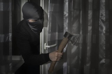 Elinde balta olan ve gözleri yarık bir şapkayla hırsız gece ay ışığında kapıdan eve gizlice girer.