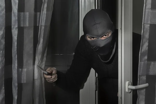 Ladro con un coltello in mano e un cappello con una fessura per gli occhi si intrufola in casa attraverso la porta di notte al chiaro di luna — Foto Stock