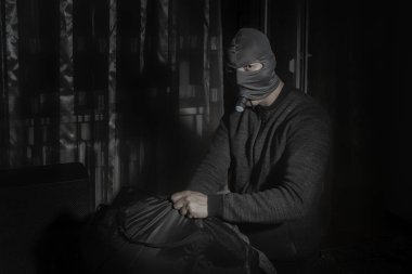 Hırsız maskeli ve odada bir el feneri ile büyük bir çanta içinde ganimet koyar