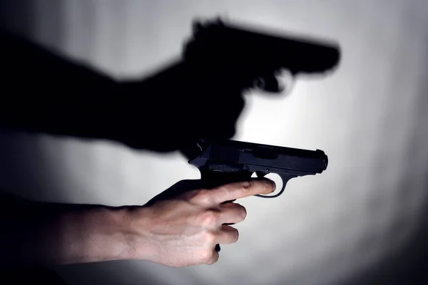 Hand with a gun on the background of a wall with a shadow from a pistol. Copy space — Stock Photo, Image