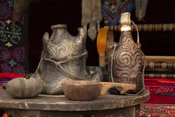 Os pratos cazaques tradicionais de bebidas feitas de madeira e couro estão em uma velha mesa de madeira em uma iurta - a casa de nômades. Close-up — Fotografia de Stock