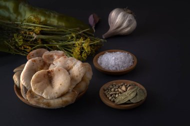 Fermantasyon için baharatile birlikte karanlık bir masada ahşap bir tabakta tuzlu mantar. Düşük anahtar.