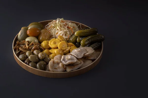 Productos fermentados repollo, pimientos, encurtidos, tomates, champiñones, calabacín, ajo en un gran plato de madera sobre una mesa oscura. Bajo perfil. Copiar espacio — Foto de Stock
