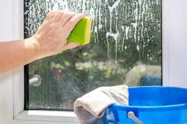 Kadının eli, sabunlu pencereyi süngerle ovalıyor.