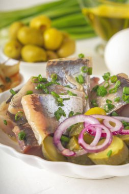 Kırmızı soğanlı turşulu ringa balığı, mayalanmış salatalık, kızarmış patates, zeytin, haşlanmış yumurta ve hafif ahşap bir masada otlar. Yakın plan.