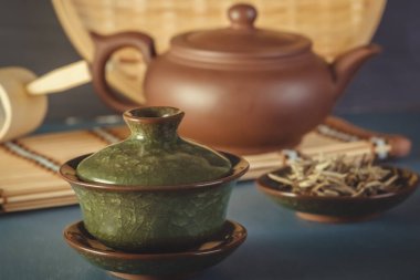 Geleneksel Asya porselen bardağı, kil çaydanlık ve çay seremonisi malzemeleri mavi masada.