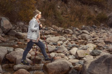 Yaşlı bir kadın dağlarda tek başına dolaşır İskandinav bastonlarıyla. Kalıcılar. Sosyal mesafe. Yerel seyahat.