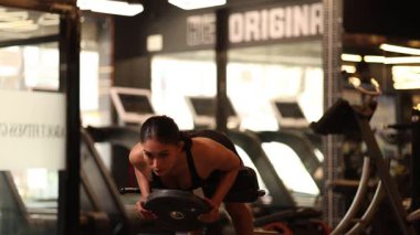 Genç bir kadın spor salonundaki bir arka eklenti makinesinde ağırlık arttırımı gerçekleştiriyor..