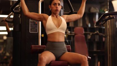Bir fitness kadını spor salonunda omuz presi yapar, gücünü gösterir ve odaklanır..
