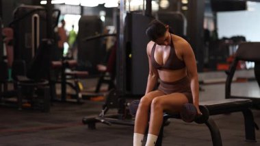 Formda bir kadın spor salonunda dambıllar kullanarak egzersiz yapar, vücuduna ve tekniğine odaklanır..