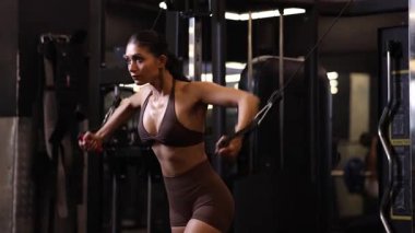 Güçlü ve formda bir kadın, antrenman sırasında kablo çapraz egzersizlerini odaklanarak ve kontrol ederek gerçekleştirir..