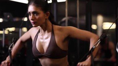Dişi bir vücut geliştirici spor salonunda göğüs kablosu keserek güç ve kontrol gösterisi yapıyor..