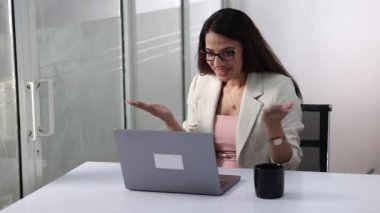 Modern bir ofisteki bir kadın, dizüstü bilgisayar kullanarak sanal bir toplantıya katılıyor..