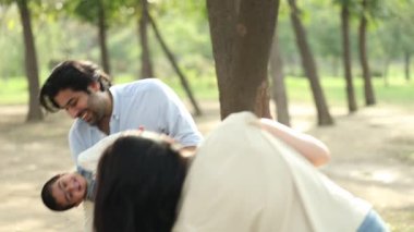 Neşeli bir aile birlikte vakit geçirir, parktaki ağaçlar arasında eğlenceli aktivitelerle meşgul olurlar..