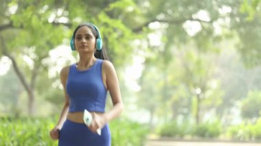 Parkta koşarken kulaklıkla müzik dinleyen mutlu sporcu kadın..