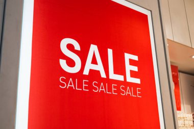 Bir mağaza vitrininde parlak kırmızı satış posteri, kalın tipografi.