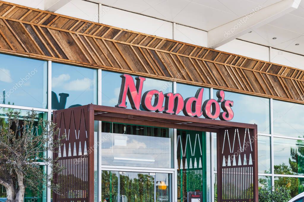 Facade of a Nandos restaurant with red logo and glass windows. London, UK, 28 July 2024
