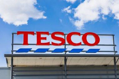 Mavi gökyüzünün altındaki süpermarketin çatısında kalın kırmızı Tesco tabelası. Londra, İngiltere, 28 Temmuz 2024