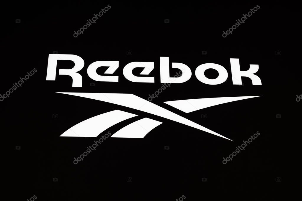 Minimal Reebok storefront sign with bold wordmark on a dark wall. London, UK, 28 July 2024