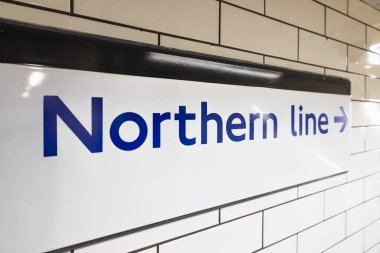 Londra metro istasyonunda beyaz fayanslı bir duvara, sağ ok ve metro yolcuları için temiz yol bulma tasarımıyla kuzey hattı tabelasını kapatın..
