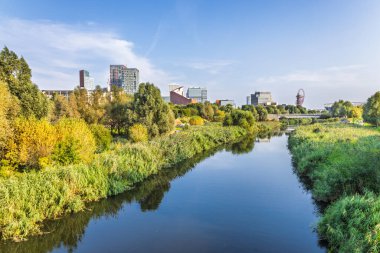 Tranquil River Lea, Stratford silueti, yemyeşil yemyeşil ve mavi gökyüzü yansımaları ile Kraliçe Elizabeth Olimpiyat Parkı 'nda kıvranıyor. Doğu Londra 'da şehir doğası.