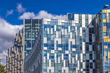 Yansıtıcı pencereler, geometrik desenler ve mavi gökyüzü olan çağdaş cam ofis cephesini kapat.