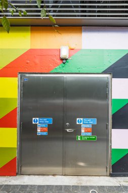 Renkli bir şehir duvarında çıkış ve güvenlik işaretleri olan paslanmaz çift yangın kapısı..