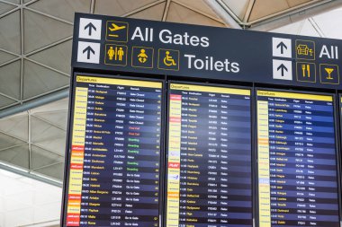Modern bir havaalanı terminalinde gidiş, geliş ve geçit yönlerini gösteren dijital uçuş bilgisini kapat. Londra, İngiltere, 11 Kasım 2024